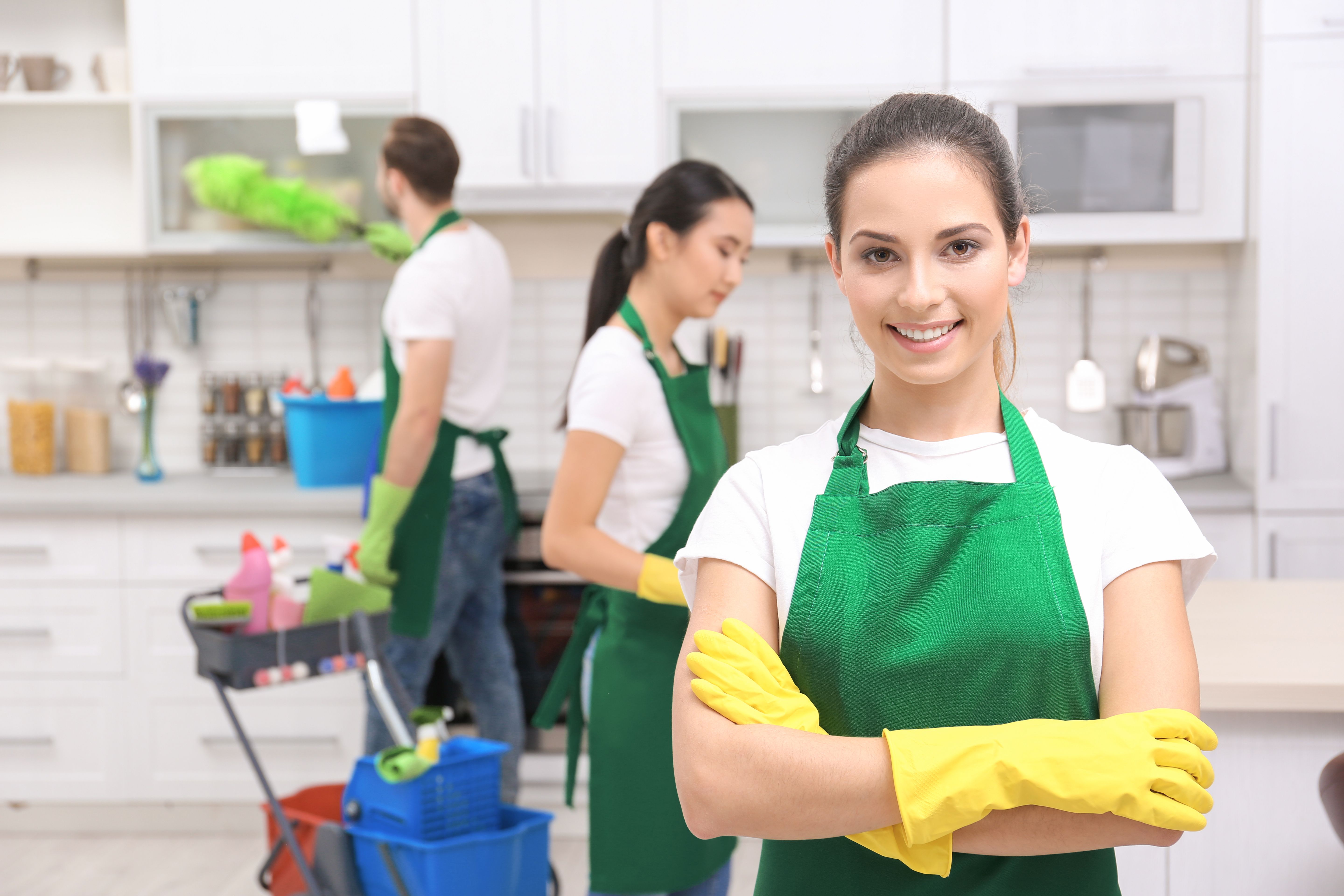 Professional commercial cleaning team in green aprons working in a kitchen